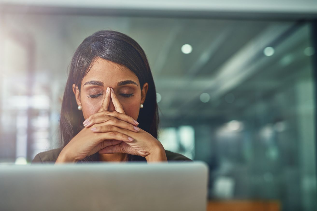 Manager at a desk, overwhelmed, hands pressed to face